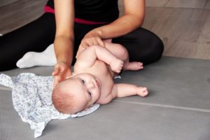 Mama masuje niemowlę na macie do ćwiczeń w jasnym pomieszczeniu.